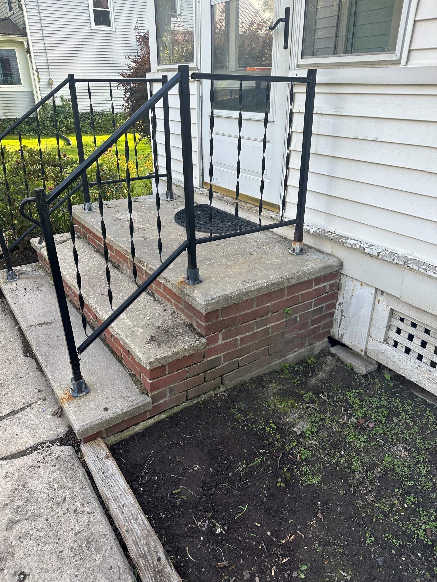Concrete front steps with black metal railings leading to a house entrance.
