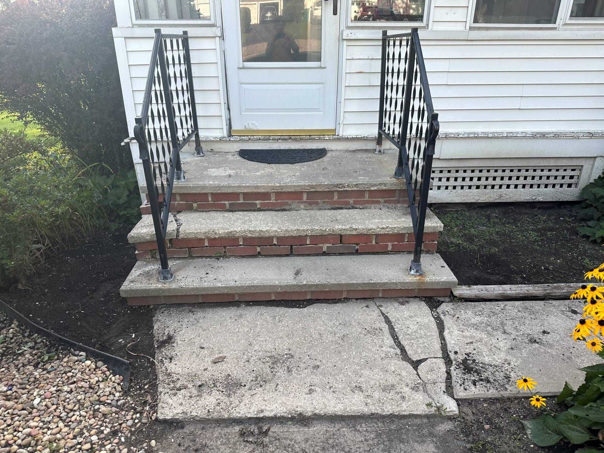 Concrete entrance steps with brick trim and black decorative metal railings leading to a house door.