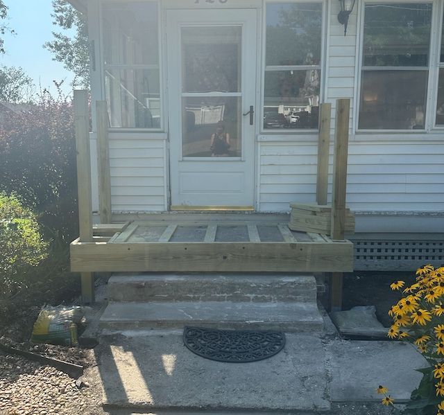 A newly built wooden porch frame with two upright support posts sits in front of the white door of a house.