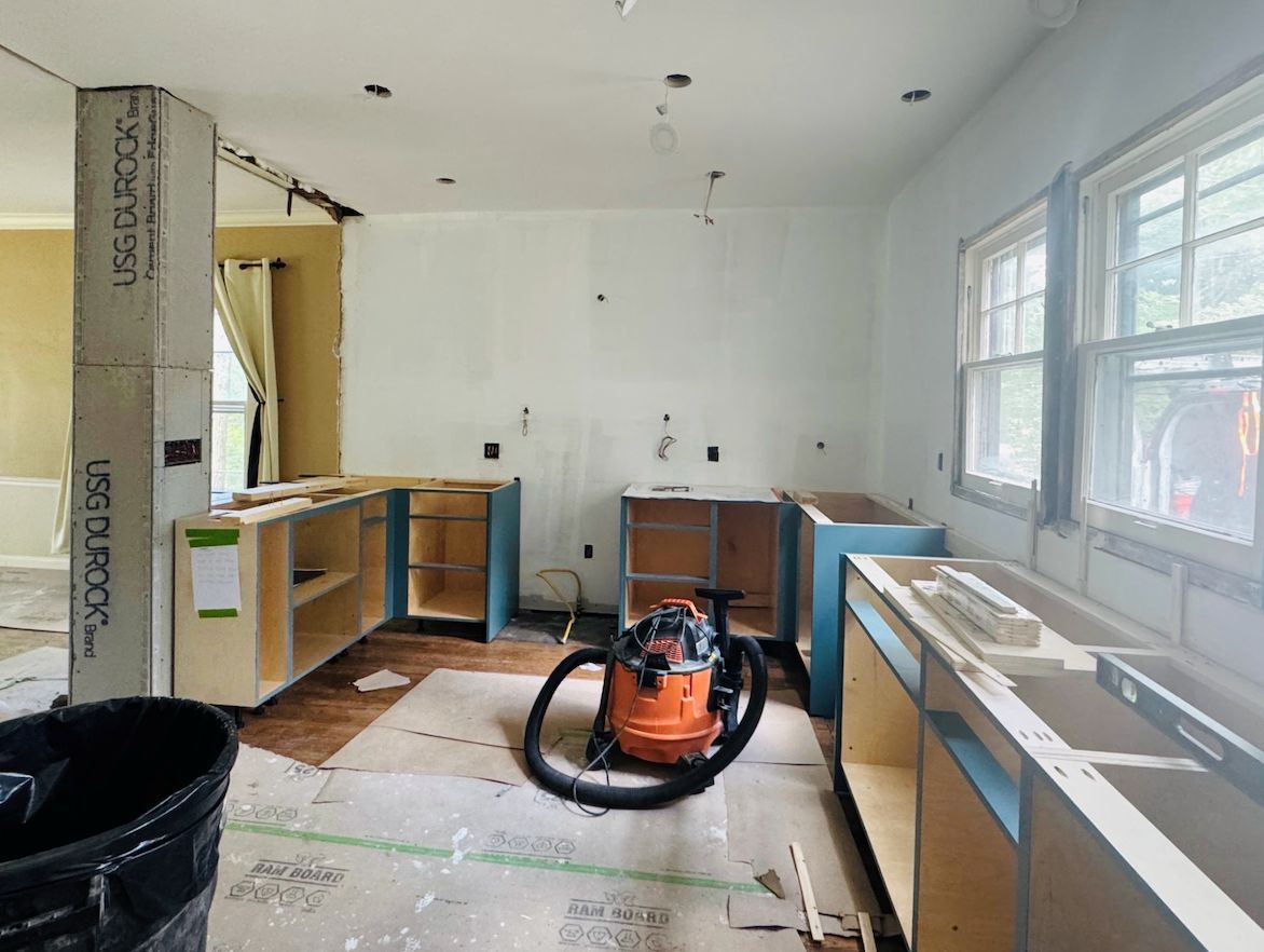 A kitchen under construction with blue unfinished cabinets, a wet-dry vacuum on the floor, and exposed wall materials.