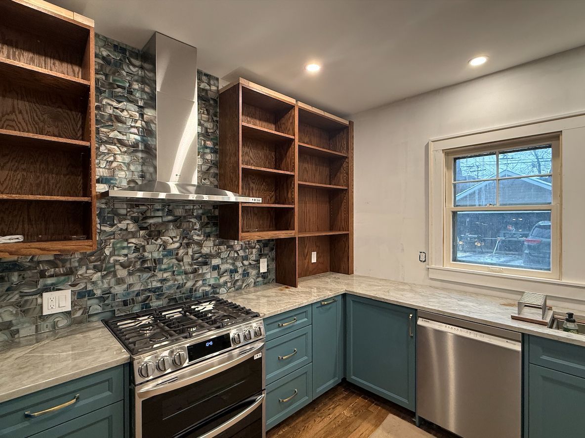 A modern kitchen with blue lower cabinets, wood open shelves, a stainless steel stove, and a blue decorative backsplash.