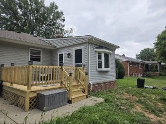 Light gray house exterior featuring a wooden deck with stairs leading down to a concrete patio.