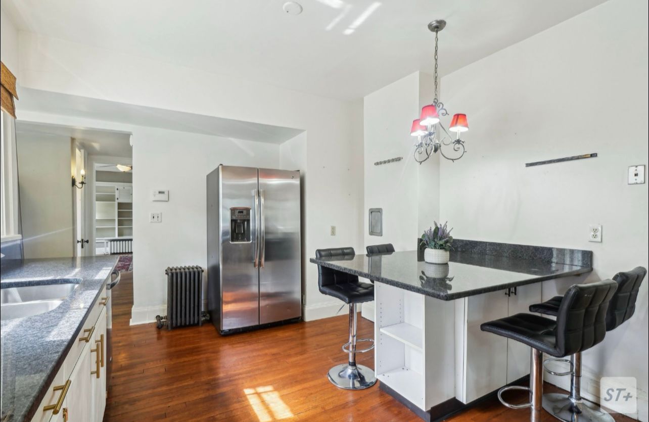 Kitchen with hardwood floors, stainless steel refrigerator, white cabinets, dark countertop, and three bar stools.