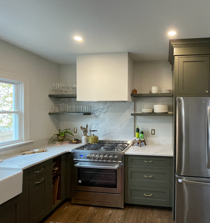 A modern kitchen with dark green cabinets, marble-patterned backsplash, white countertops, and a stainless steel stove.