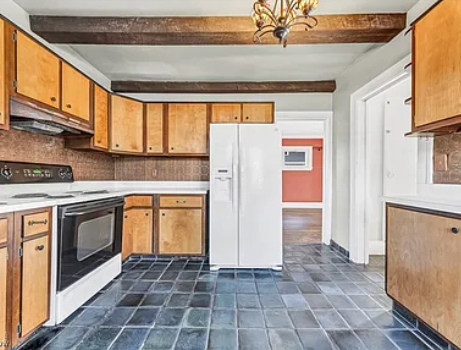 A kitchen with wood cabinets, dark tiled floors, a white refrigerator, and exposed wooden ceiling beams.