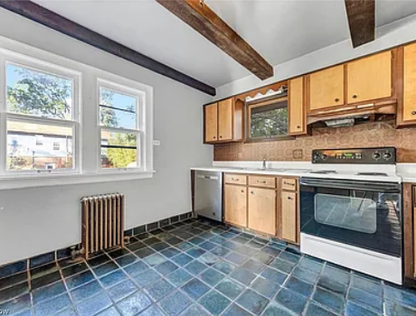 A kitchen with blue tile floors, light wood cabinets, an oven, a dishwasher, and exposed wood ceiling beams.