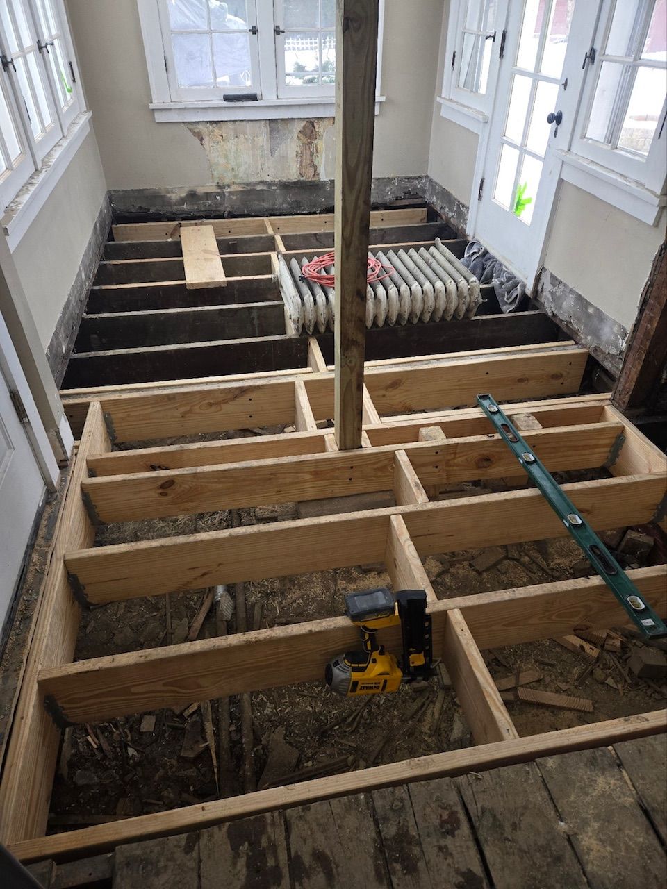 A construction view of a sunroom floor being rebuilt with new wooden joists and a central support beam.