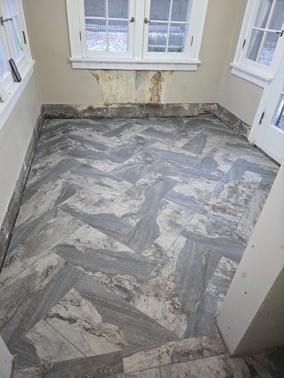 A room with unfinished walls and a grey herringbone-patterned stone floor, showing signs of renovation.