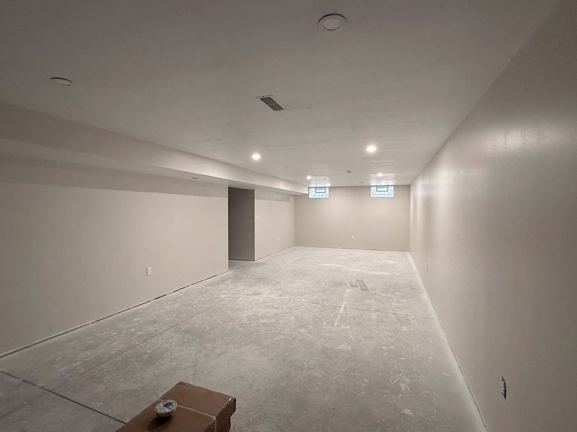 A spacious, empty basement with light gray walls, recessed ceiling lights, and a concrete floor.