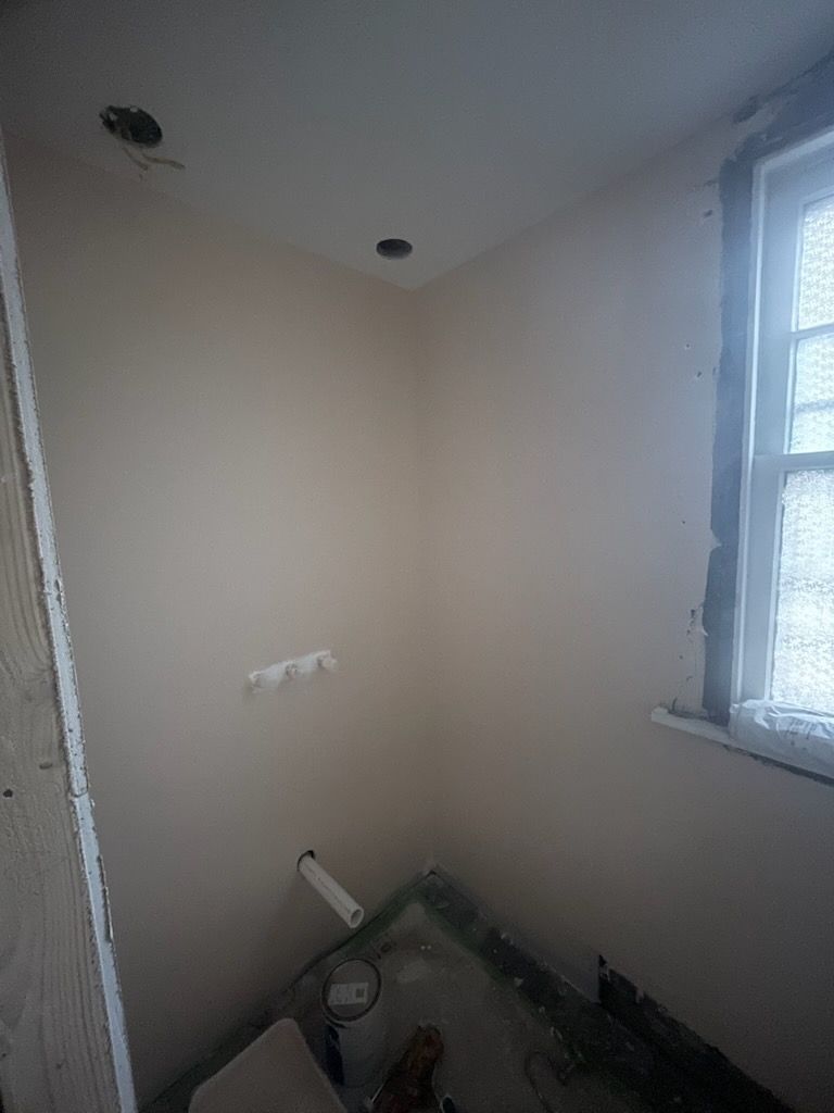 A small, empty bathroom corner under renovation with unfinished walls, a single window, and exposed plumbing pipes.