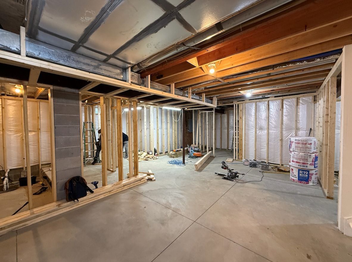 Unfinished basement construction with framed wooden walls, concrete floors, and visible insulation against exterior walls.