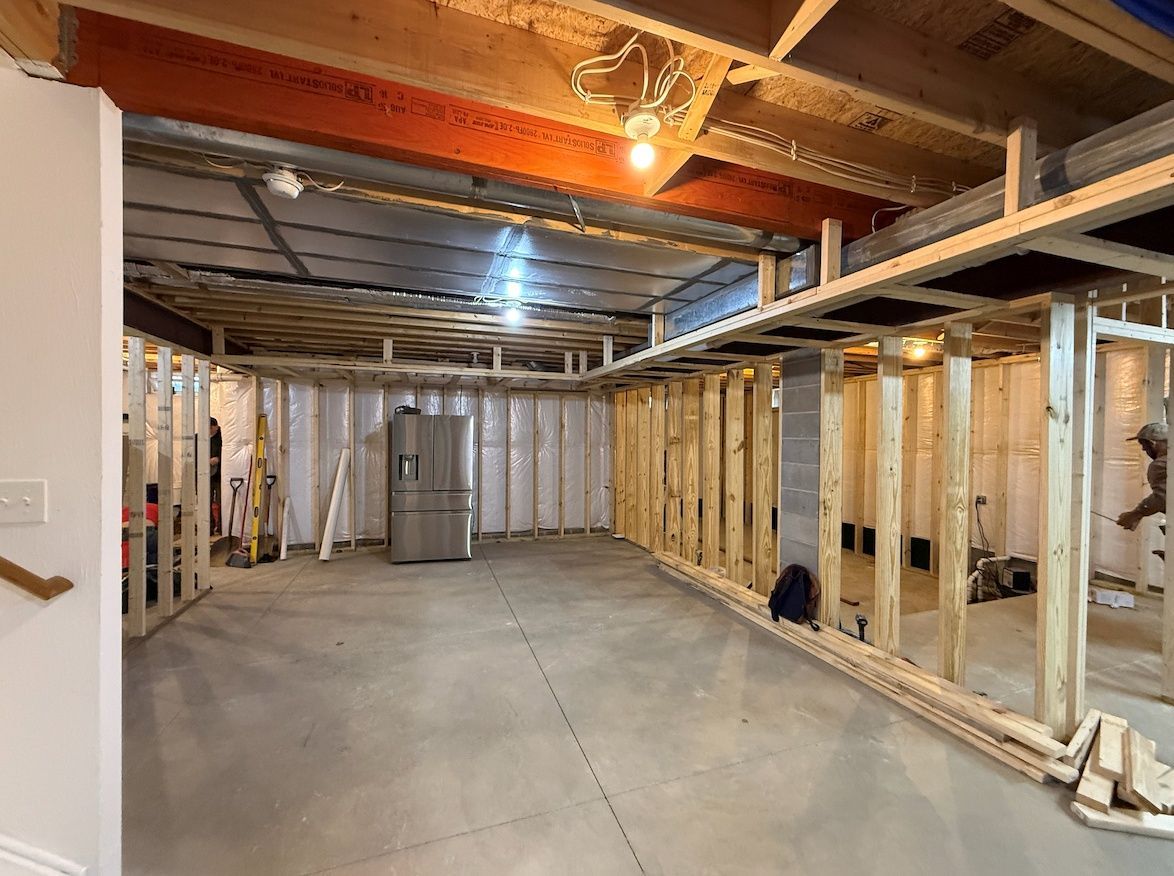 Unfinished basement under construction with exposed wood framing, concrete floor, and silver water heater.