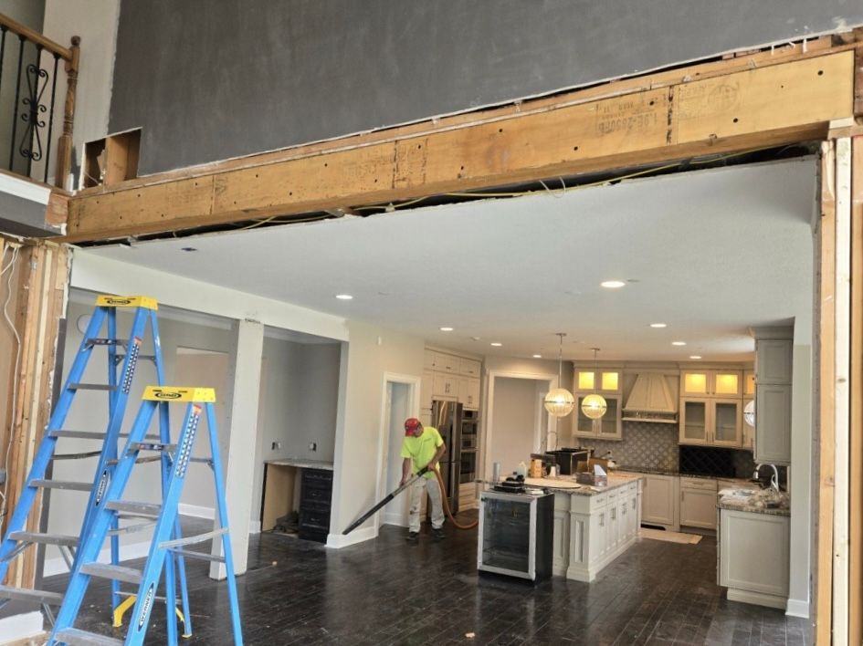 A worker cleans a renovation site featuring an exposed structural beam opening up a kitchen and living area.