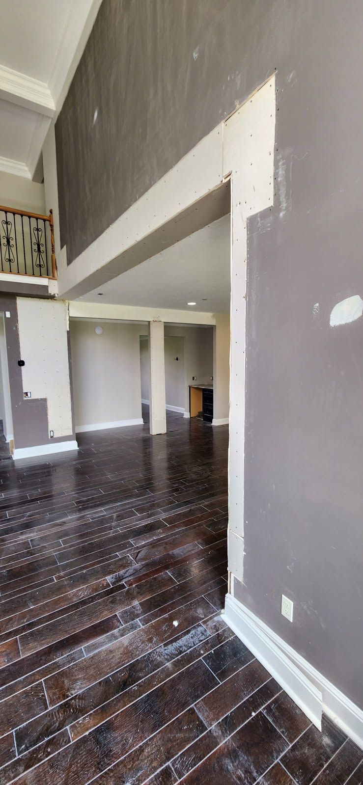 A view of an unfinished home interior featuring dark grey walls, exposed drywall at the edges, and dark wood flooring.