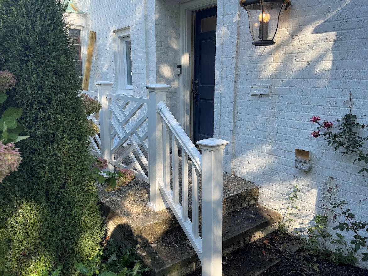 A dark blue front door with a white railing and stairs on a white brick building, with a wall lantern above.