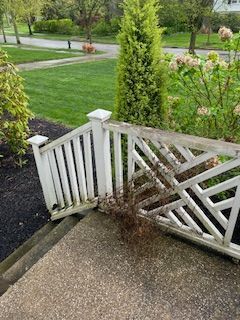 A white wooden staircase railing with lattice detail, partially obscured by a dead shrub, on an outdoor concrete patio.