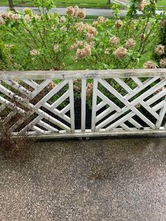 A white, decorative lattice railing stands in front of a blooming hydrangea bush on a gray concrete patio.