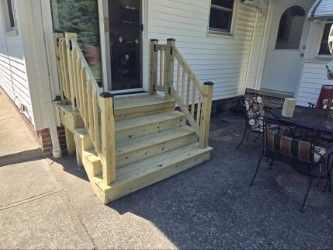 Newly constructed wooden steps with railings leading to a white house door on a paved patio.