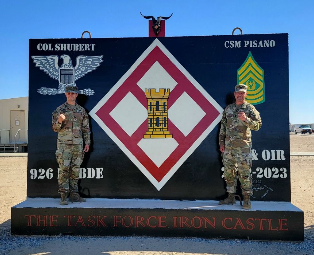 Two soldiers stand before a large sign for Task Force Iron Castle featuring the 926th Engineer Brigade emblem.