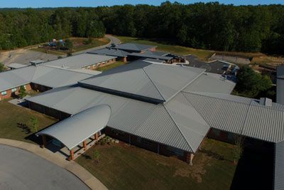 An aerial view of a large school building with a metal roof surrounded by trees.