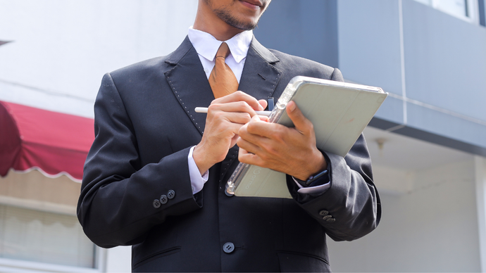 A person in a business suit holding a digital tablet and stylus while working outside a building.