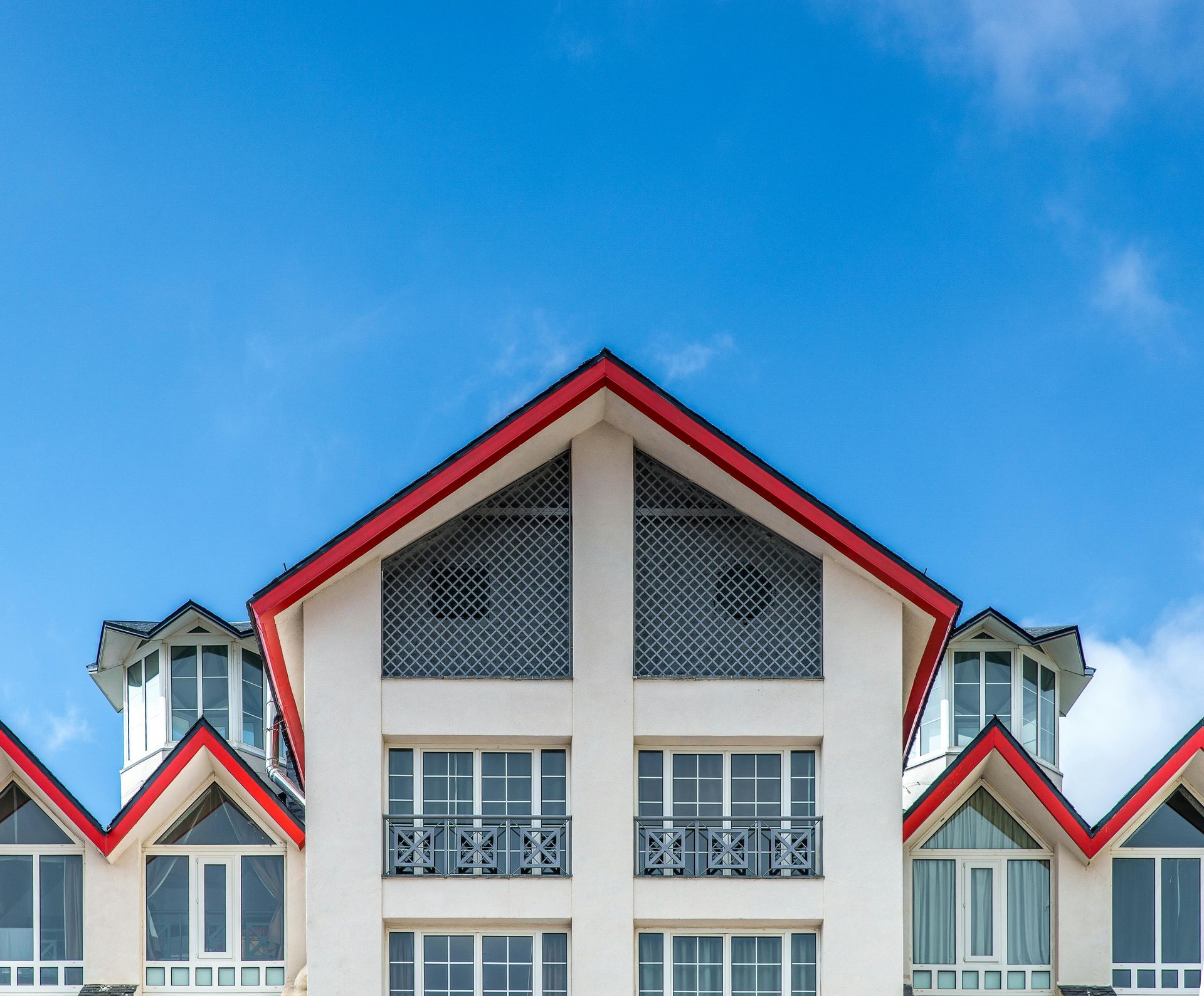 A low-angle view of a white, multi-story building with red-trimmed gable roofs under a bright blue sky.