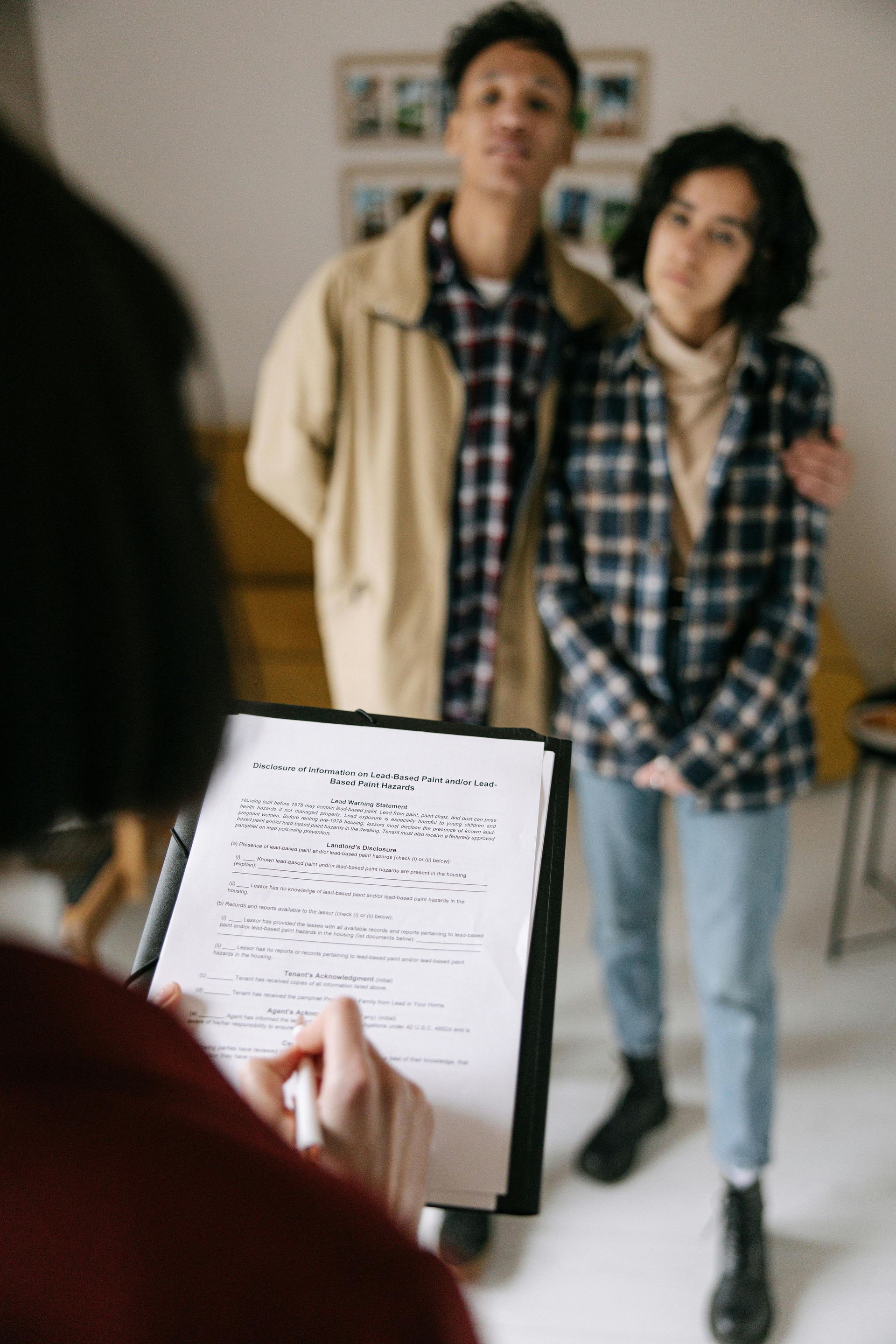 A person holds a clipboard with notes while standing before two individuals, one with an arm around the other.