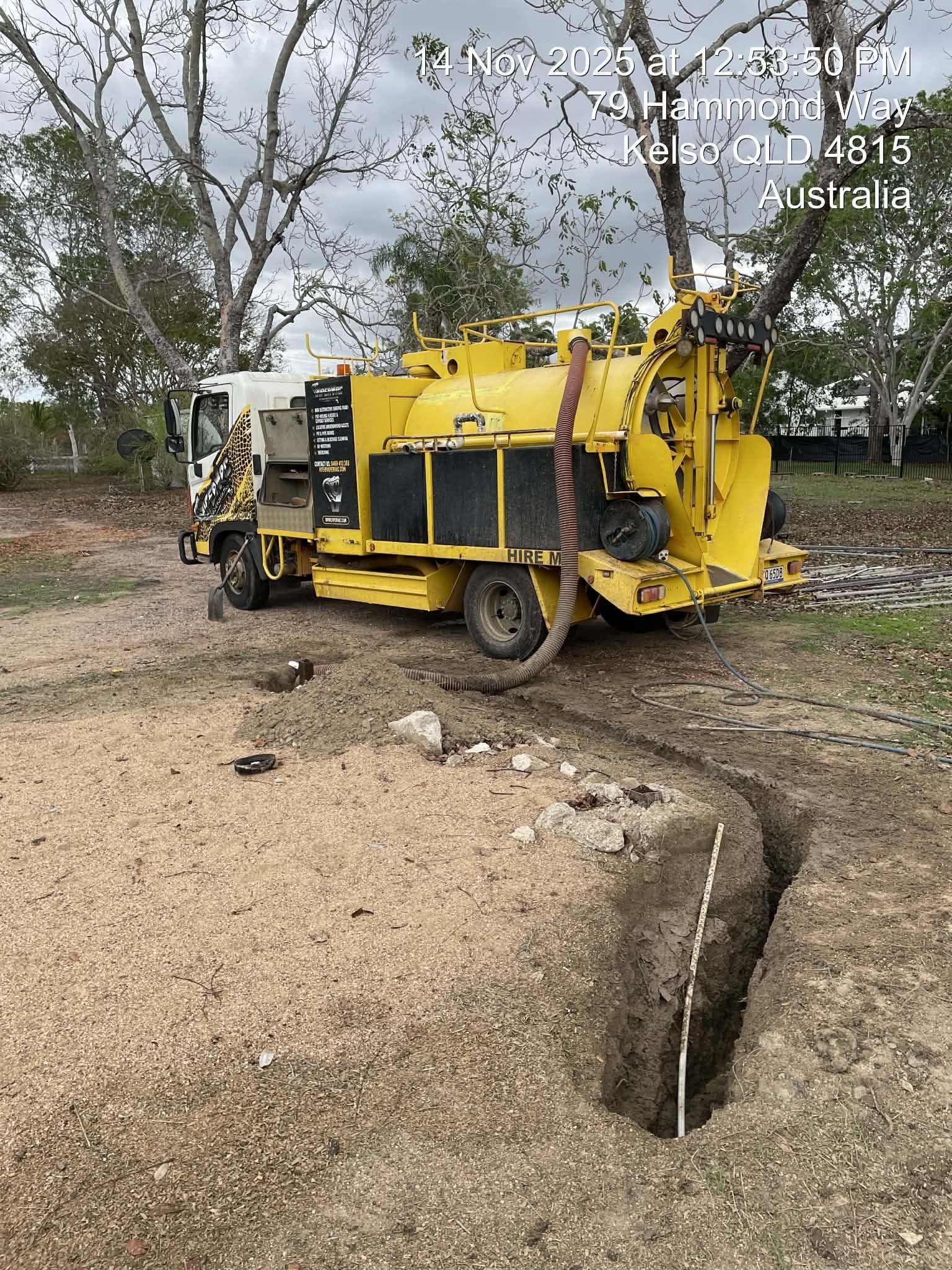Yellow utility truck beside a cracked gravel road and large erosion ditch in a wooded area