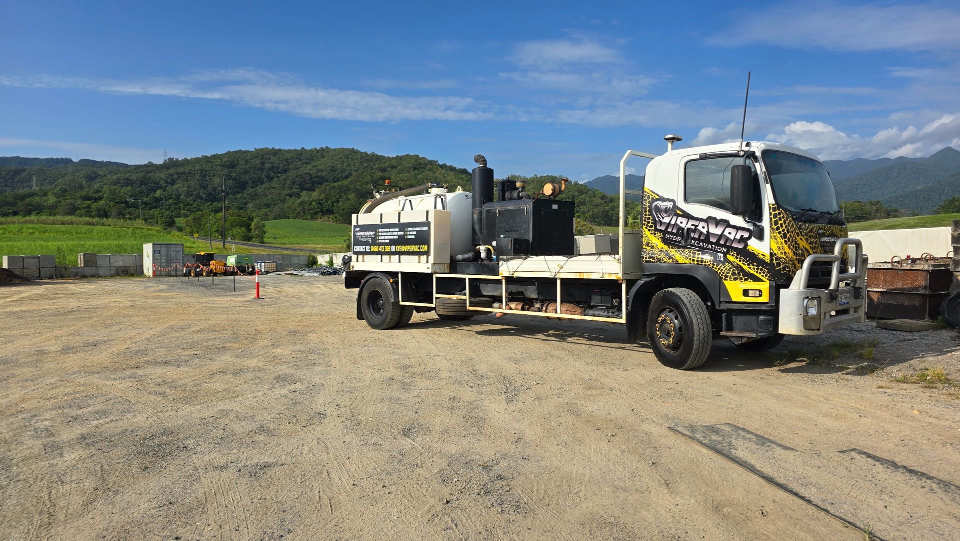 White flatbed truck on a gravel lot with mountains and green hills in the background