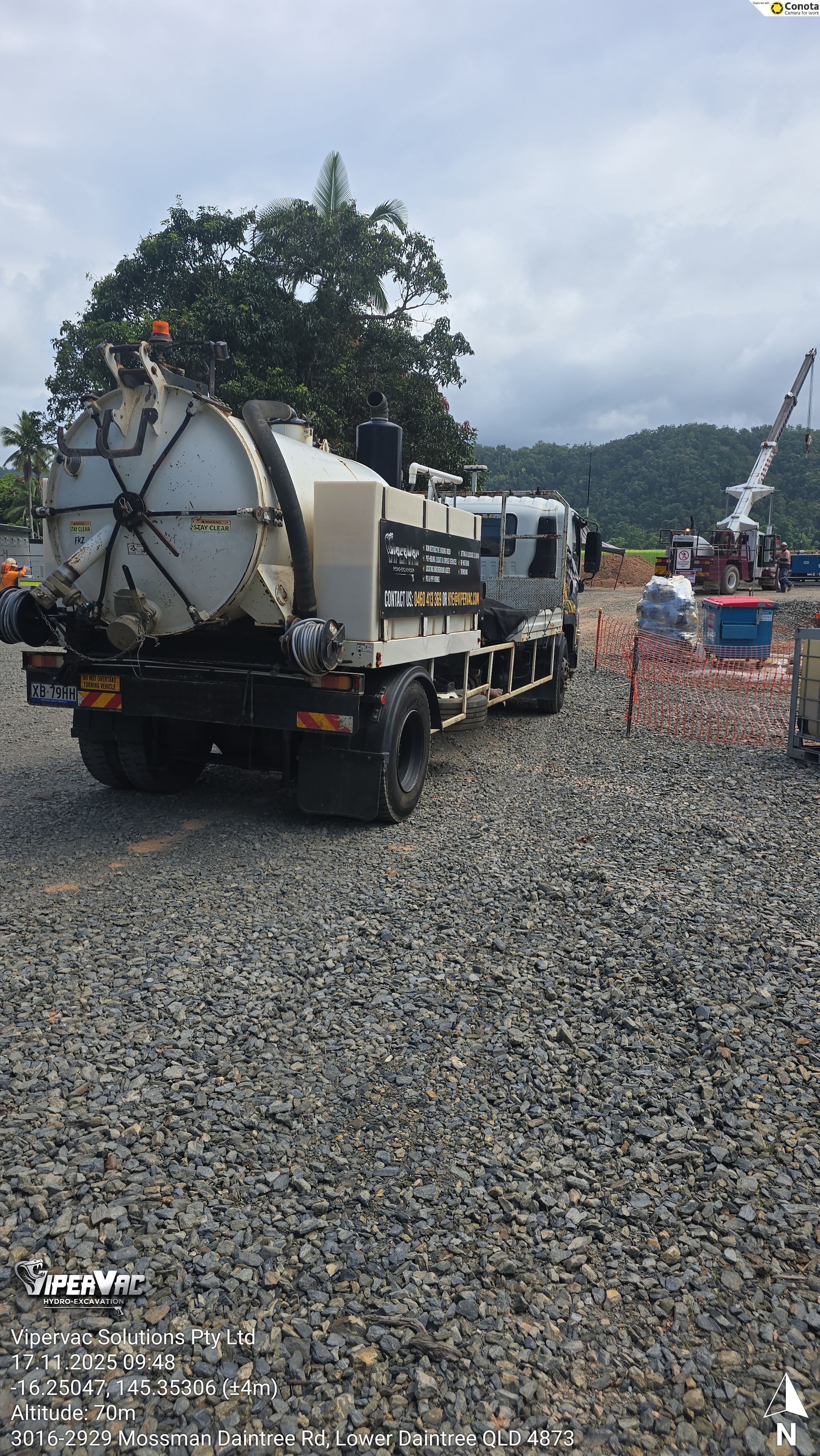 White tanker truck on a gravel road at a construction site, with hills and cloudy sky in the background
