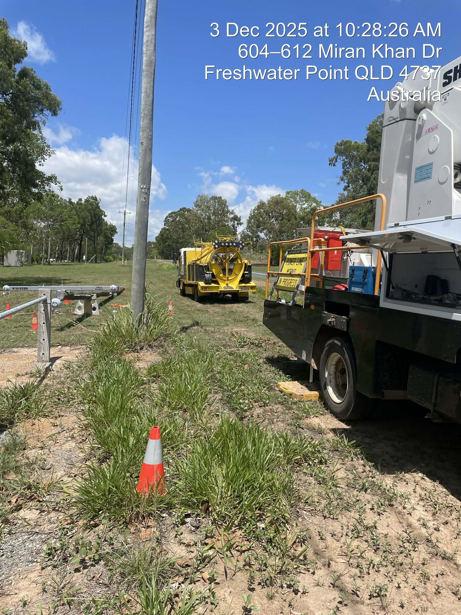 Roadside construction work with yellow machinery and a truck beside a building on a sunny day