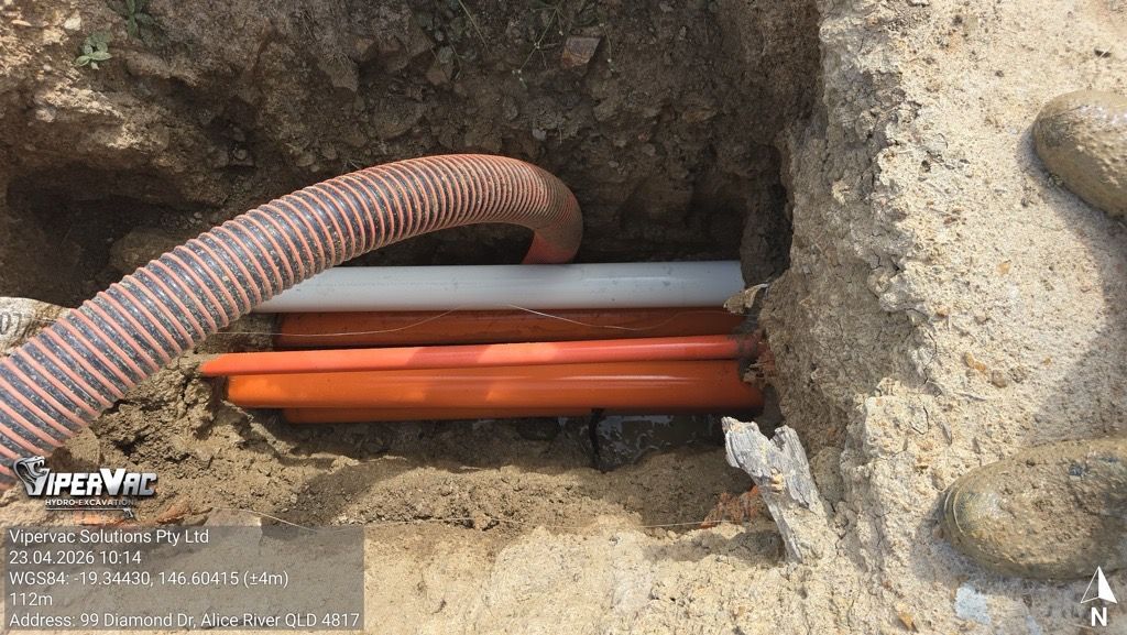 Orange cables in a dirt trench beside a pink corrugated conduit, with a small concrete opening nearby
