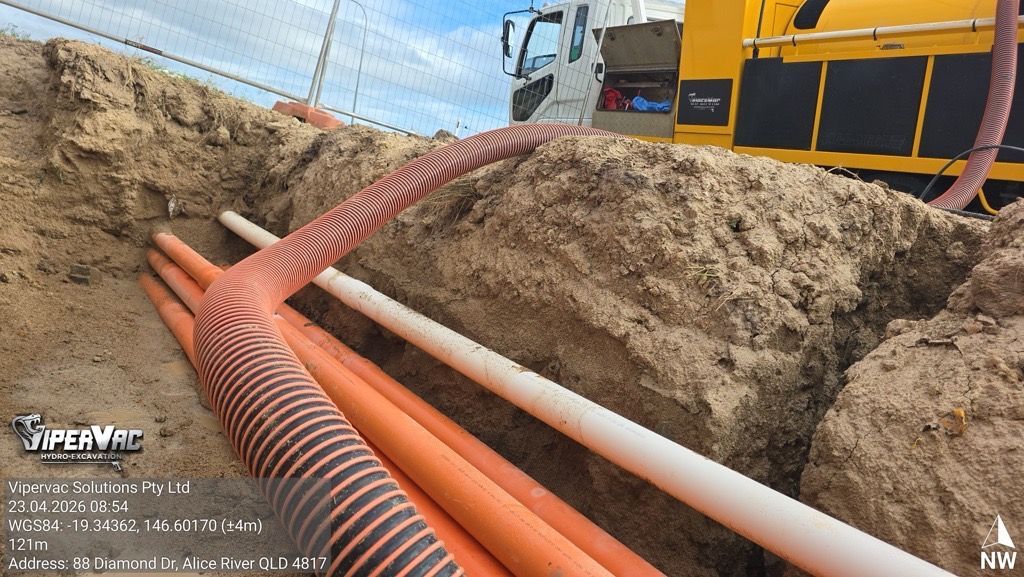 Orange hoses in a dirt trench beside heavy machinery at a construction site