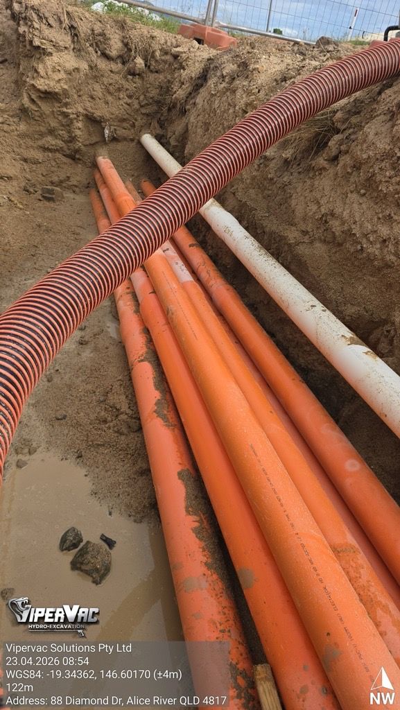 Orange and white utility pipes laid in a trench with striped safety barrier tape.