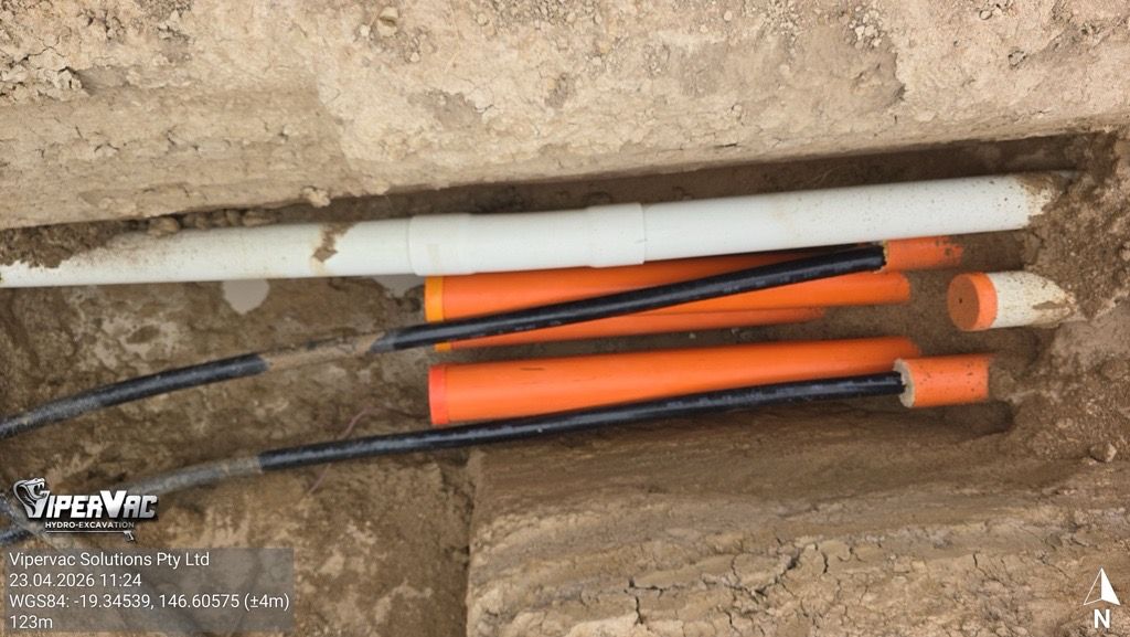 Three orange and black utility tools lying in a narrow trench beside a white pipe.