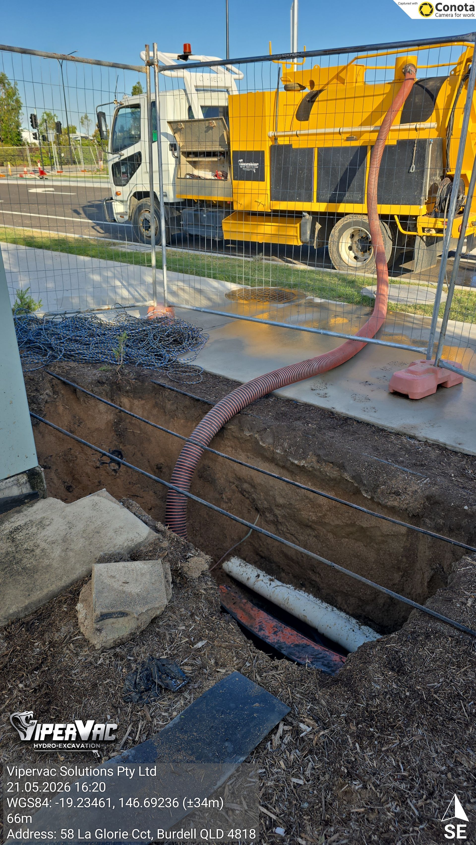 Yellow construction truck beside a deep trench with exposed pipes and equipment at a roadwork site