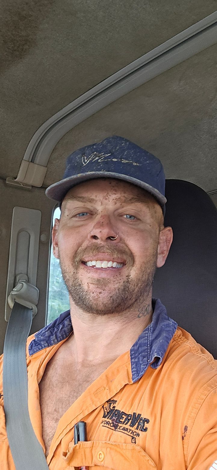 Smiling worker in orange hi-vis shirt and navy cap sitting in a vehicle cab