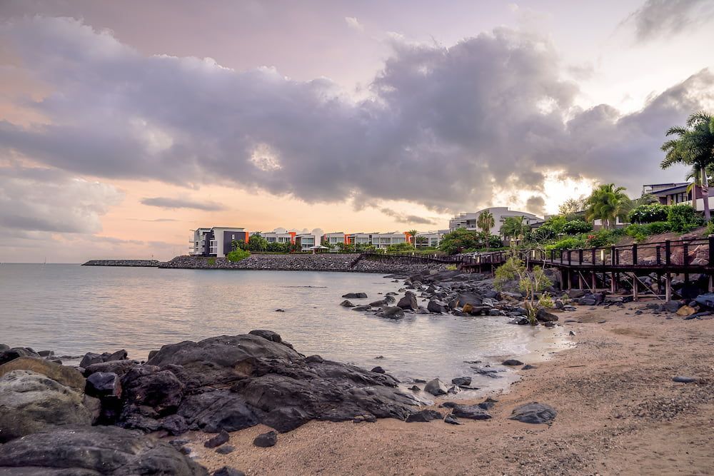 A Beach With Rocks And A City In The Background At Sunset — ViperVac Solutions PTY LTD in Airlie Beach, QLD