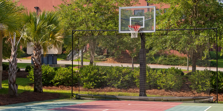 Basketball hoop on an outdoor court with trees and buildings in the background.