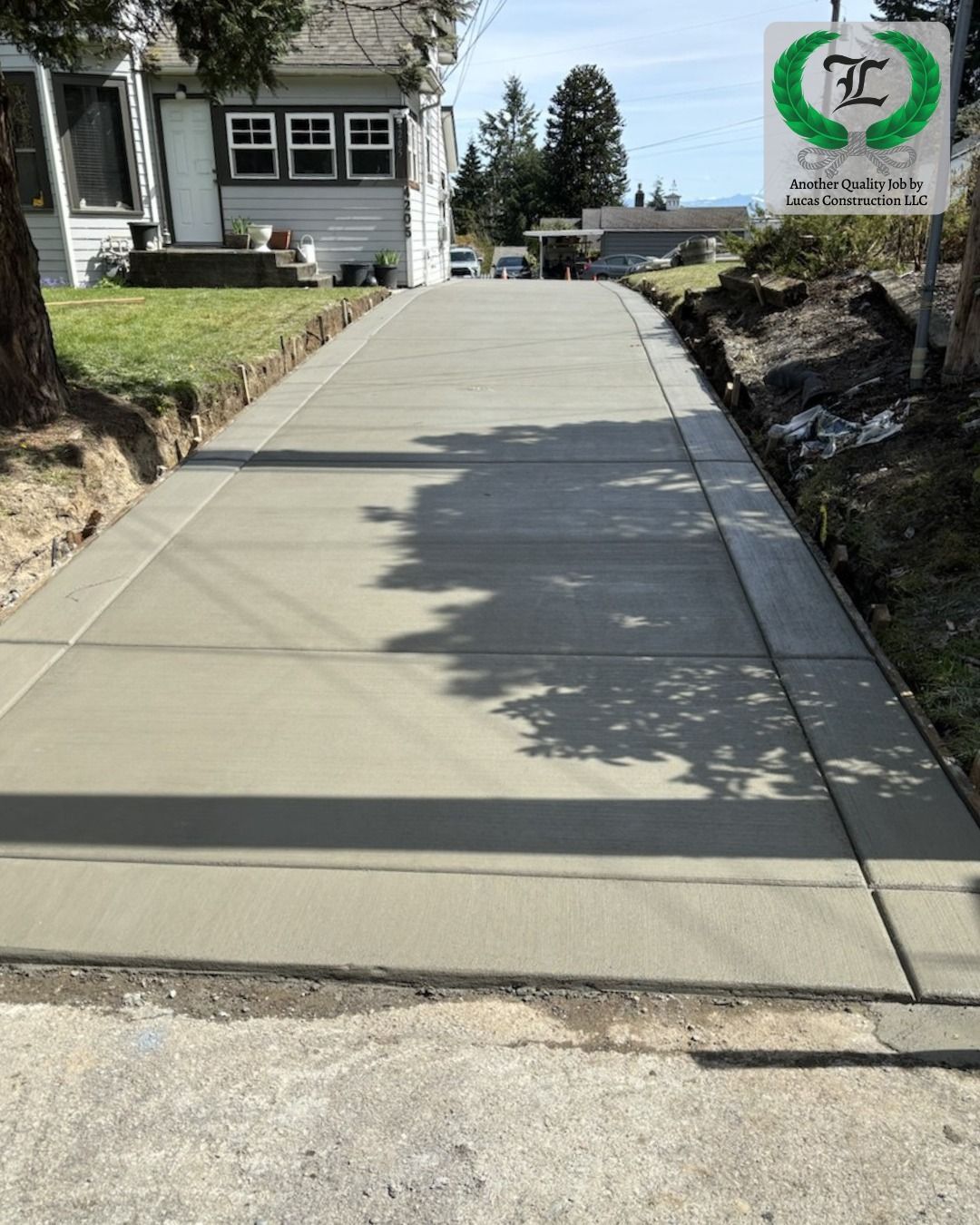 Concrete pathway with gravel borders, leading uphill. A house and trees are in the background.