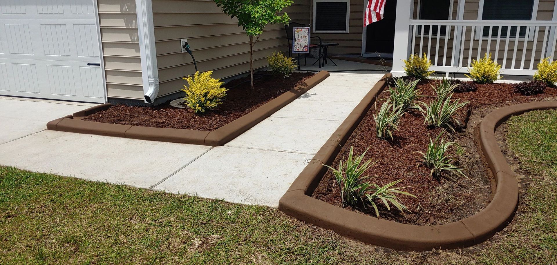 Brown concrete landscape edging borders a walkway and flowerbeds in front of a house.