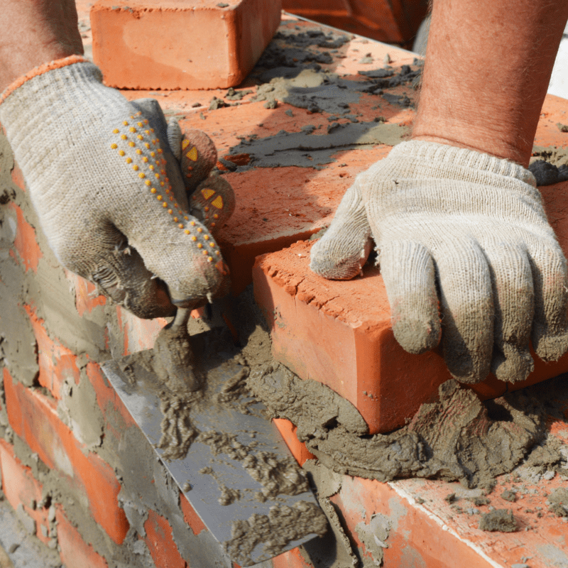 a person wearing gloves is working on a brick wall