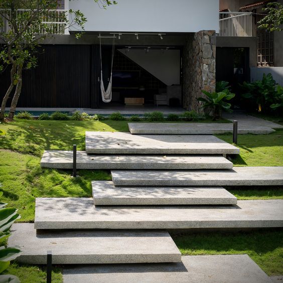 Concrete steps leading up to a modern house with a swing, surrounded by green grass.