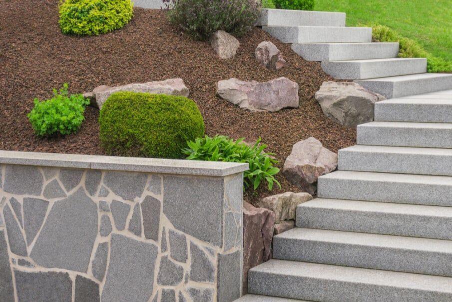 Stone staircase and retaining wall with landscaped hillside and plants.