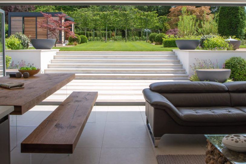 Modern home interior opens to a terraced garden with lawn, steps, and decorative plants.