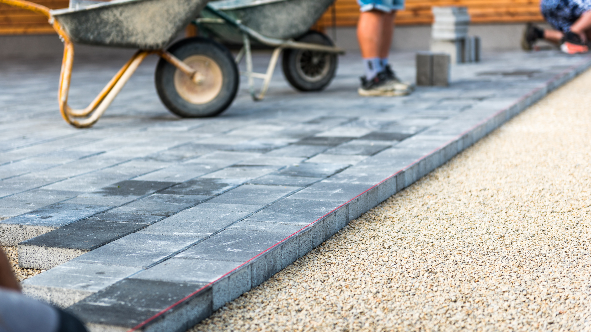 Construction worker installing pavers on gravel base with wheelbarrow.
