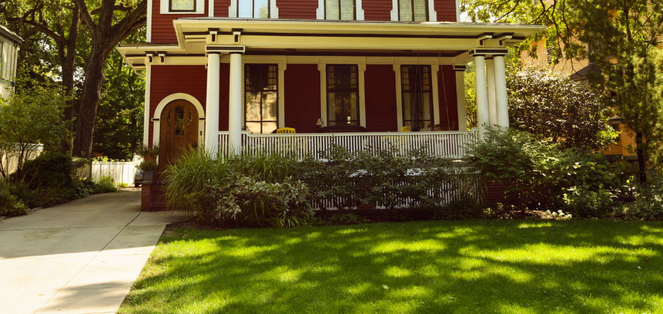 A red Victorian house with a porch and green lawn on a sunny day.