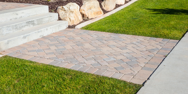 Brick walkway surrounded by green grass and concrete steps leading up to rocks.
