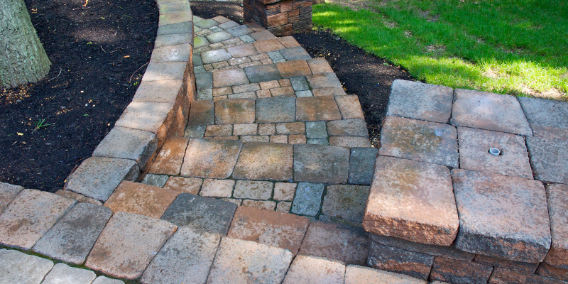 Stone steps with retaining walls, surrounded by mulch, grass, and a tree trunk.
