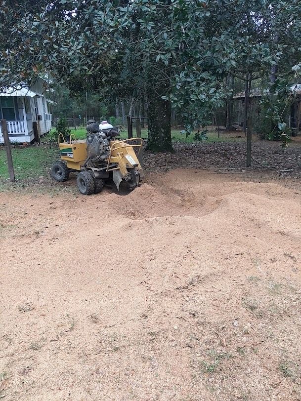Yellow tractor digging dirt in a yard beside trees and a house